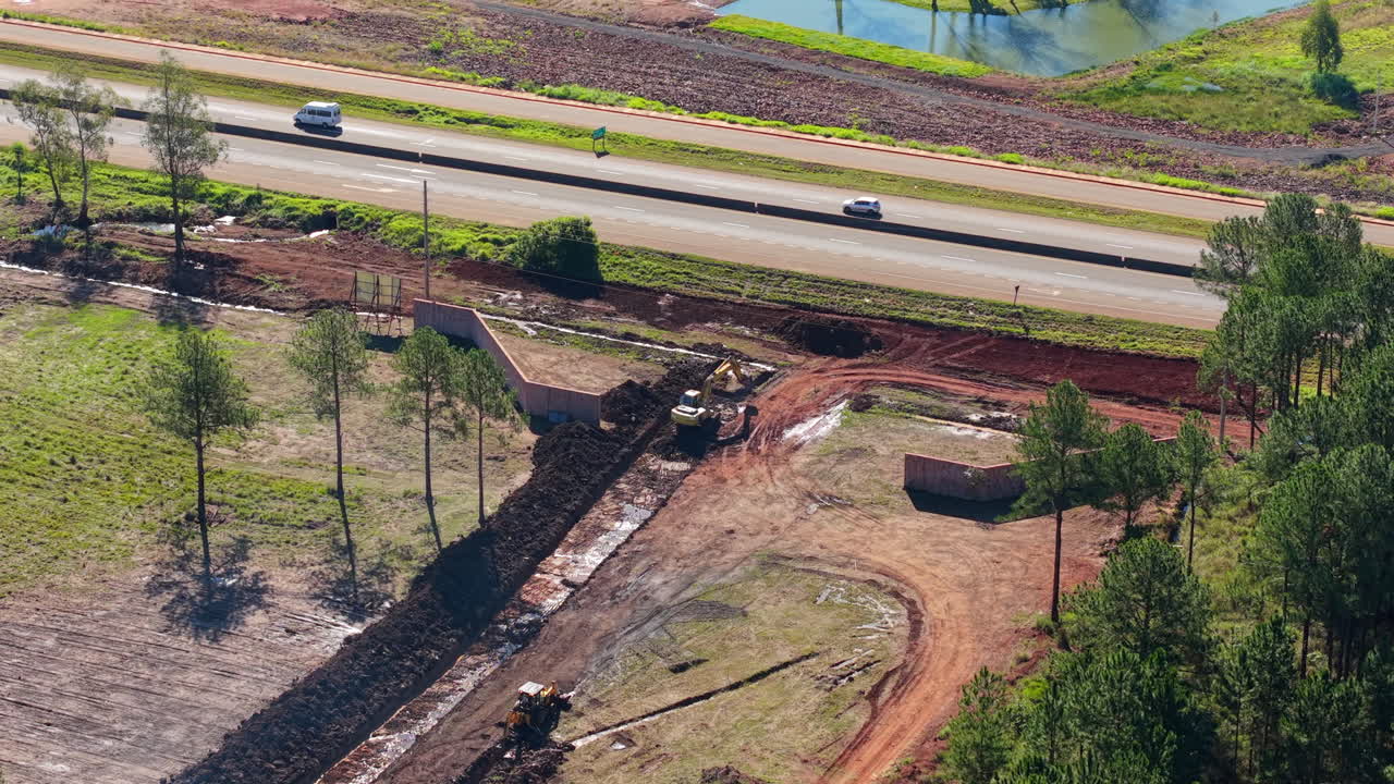 Construction site with machinery clearing earth near road, aerial view, sunny day