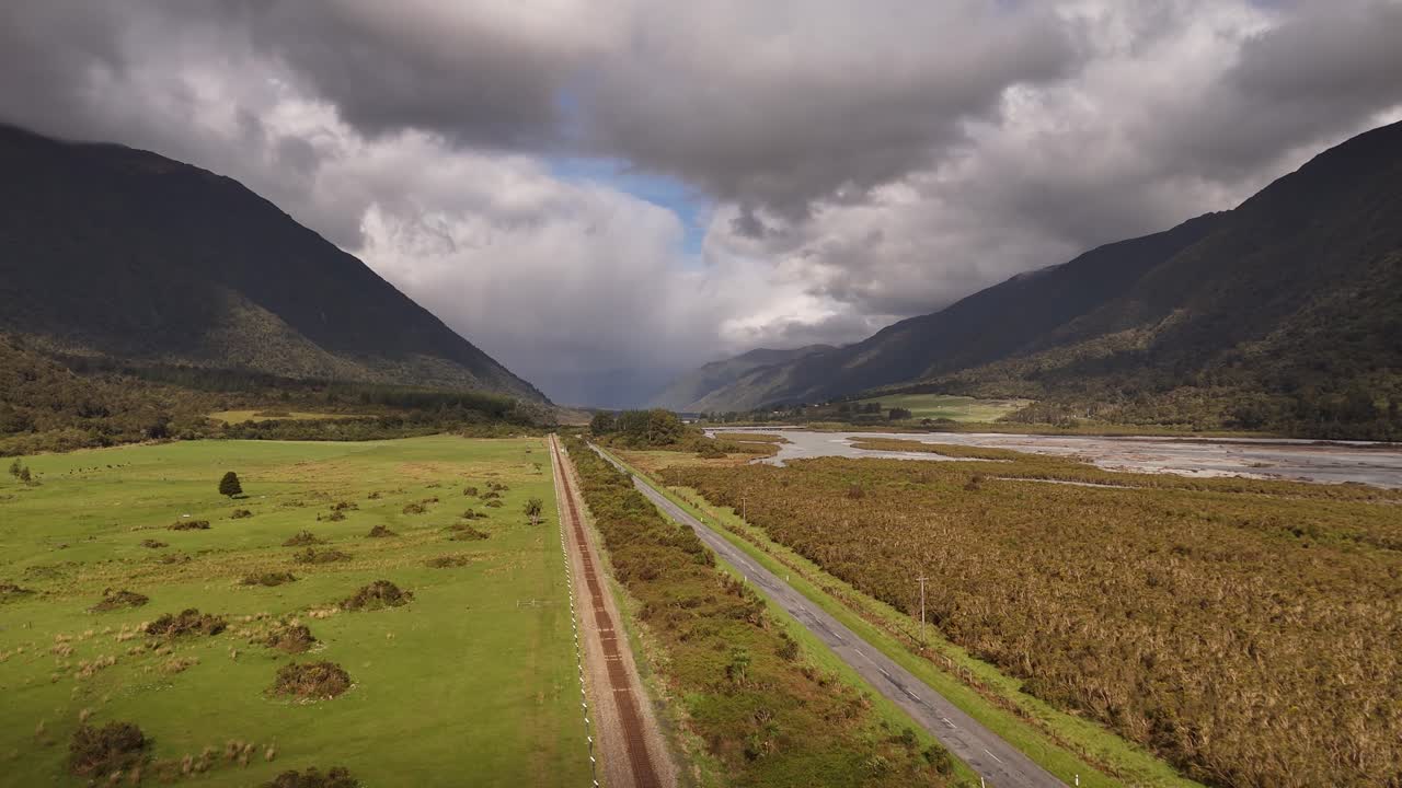 Volo di drone su strada vuota e binari ferroviari che attraversano una remota valle di montagna in Nuova Zelanda. Ripresa aerea in avanti, con spazio per il testo.
