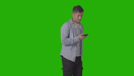 Studioaufnahme-Eines-Leger-Gekleideten-Jungen-Mannes,-Der-Sein-Handy-Auf-Green-Screen-2-Prüft