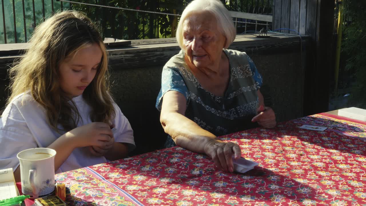 Grandma teaching family children how to play card game on summer patio table