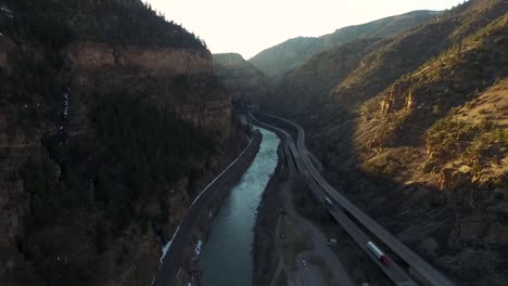 tiro aéreo de un dron volando hacia atrás en un cañón junto a una carretera con un río debajo