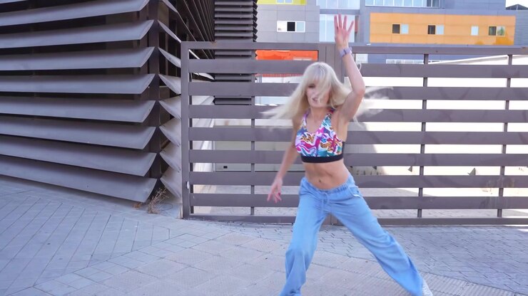 A woman dancing energetically outside in a vibrant crop top and jeans exuding confidence and style