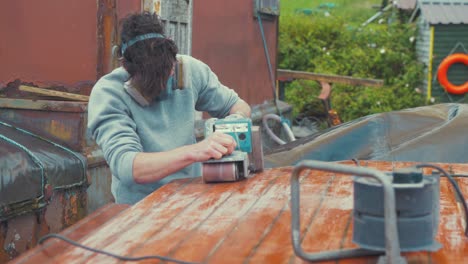 male youth belt sanding roof planking of wooden boat