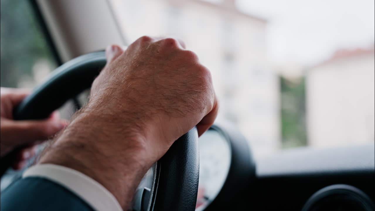 Close up of a man's hands on a steering wheel, driving a car on the road