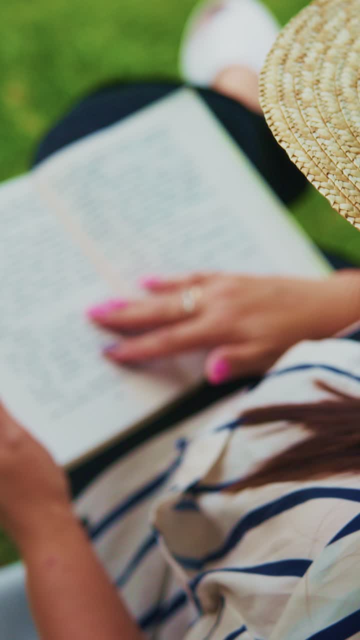 Lettura pomeridiana rilassante: primo piano di una persona che si gode un libro mentre indossa un elegante cappello di paglia in un lussureggiante ambiente verde