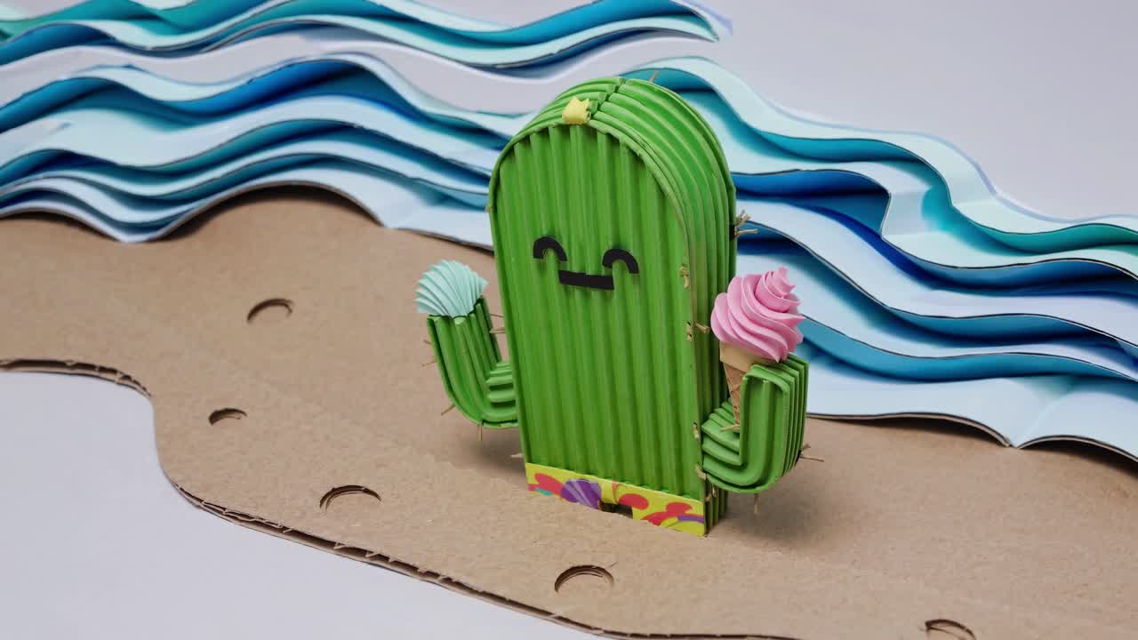 Quirky handmade cactus character enjoying ice cream cones on a miniature cardboard beach with layered paper waves, creating a whimsical and summery scene