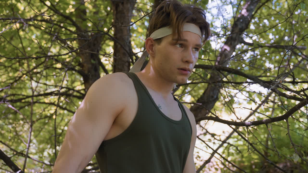 tourist backing into massive forest tree with tangled branches scanning undergrowth with alert gaze, bandana tied around head, sunlit leaves casting dappled shadows across muscular shoulder, tank top
