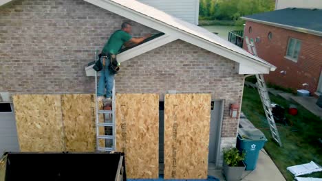 construction worker repairing the exterior of a brick house, standing on a ladder and working on the roof area above the garage."