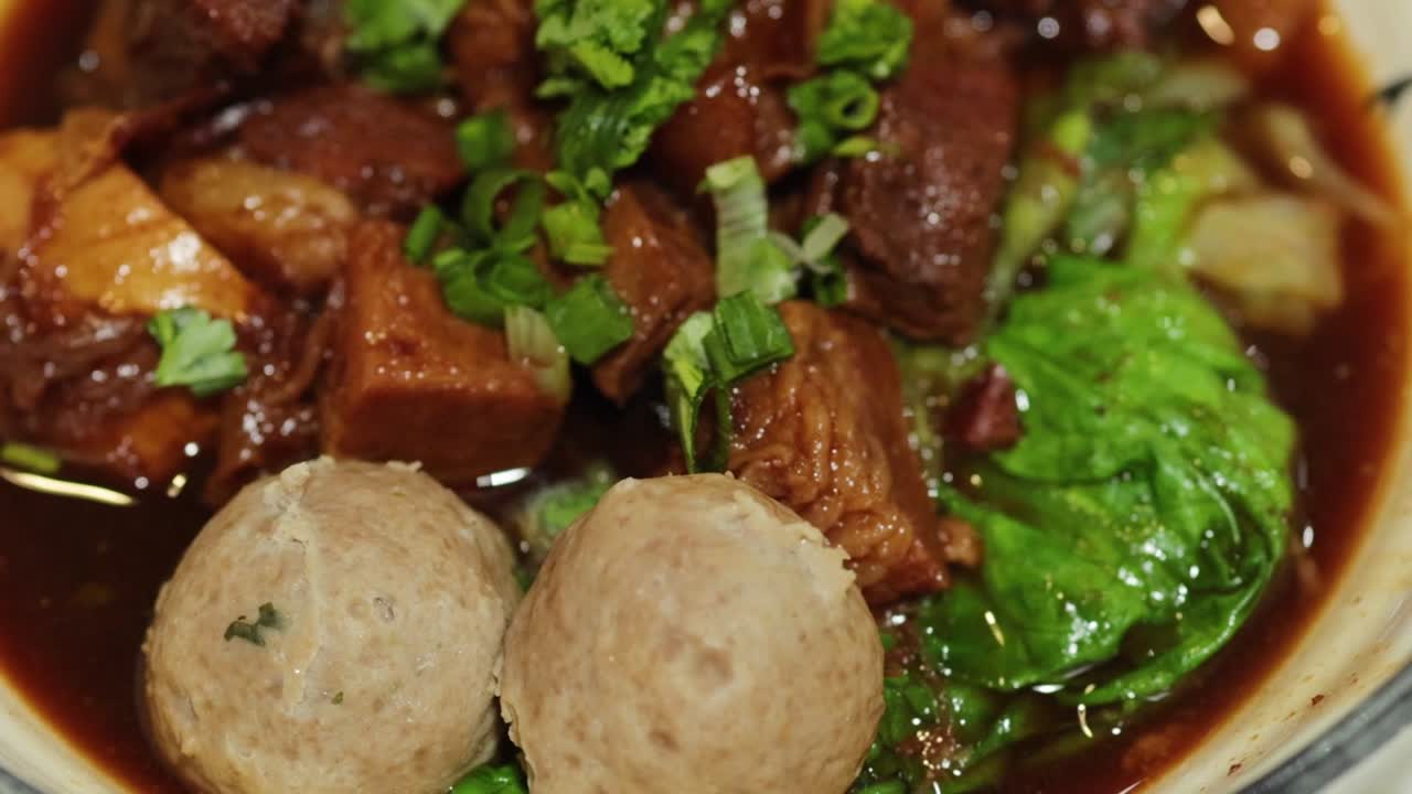 A close-up of a rich beef stew featuring meatballs, fresh greens, and savory broth.
