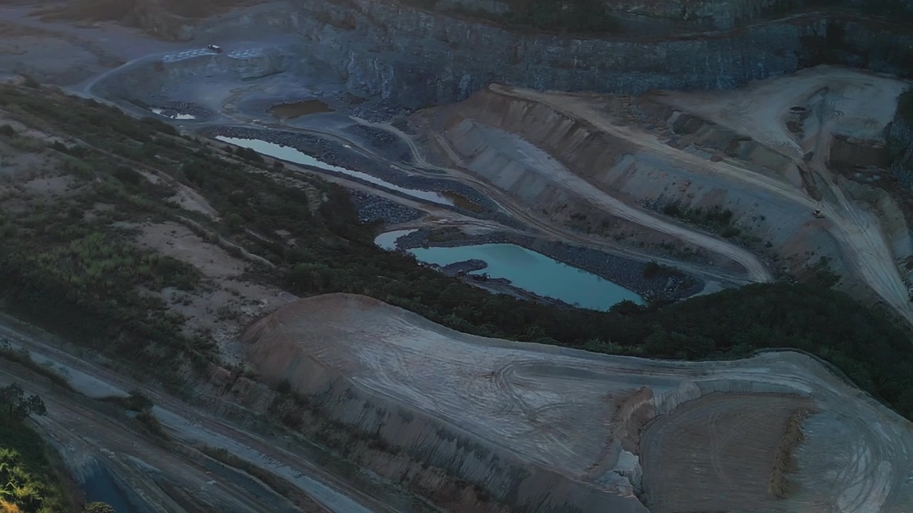 Mining excavation site in Brasília Distrito Federal Brazil showing terraced quarry walls, haul roads, exposed geology and water retention ponds during orbit establishing drone aerial shot