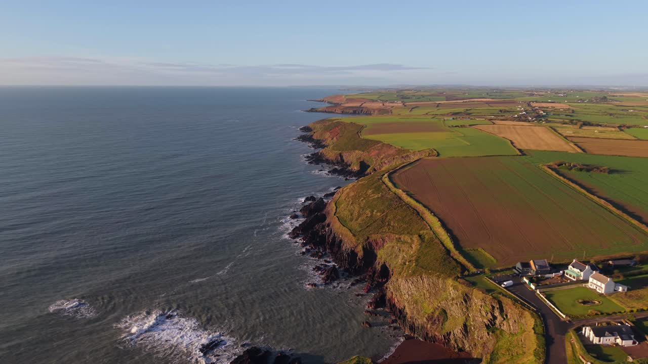 A rocky coastline with green fields, cliffs, and blue sea in Ballycotton, County Cork