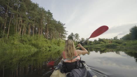 static shot of a blonde caucasian girl on her back paddling a kayak on a forest river