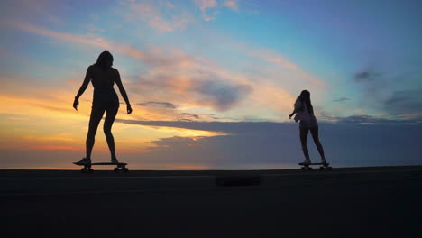 amid the enchanting hues of a sunset, two friends donning shorts engage in slow-motion skateboarding on a road. mountains and a scenic sky provide the setting