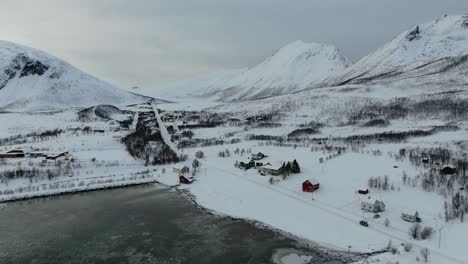 drone view in tromso area in winter flying over a snowy landscape surrounded by the sea and a frozen port with boats and white mountains in norway