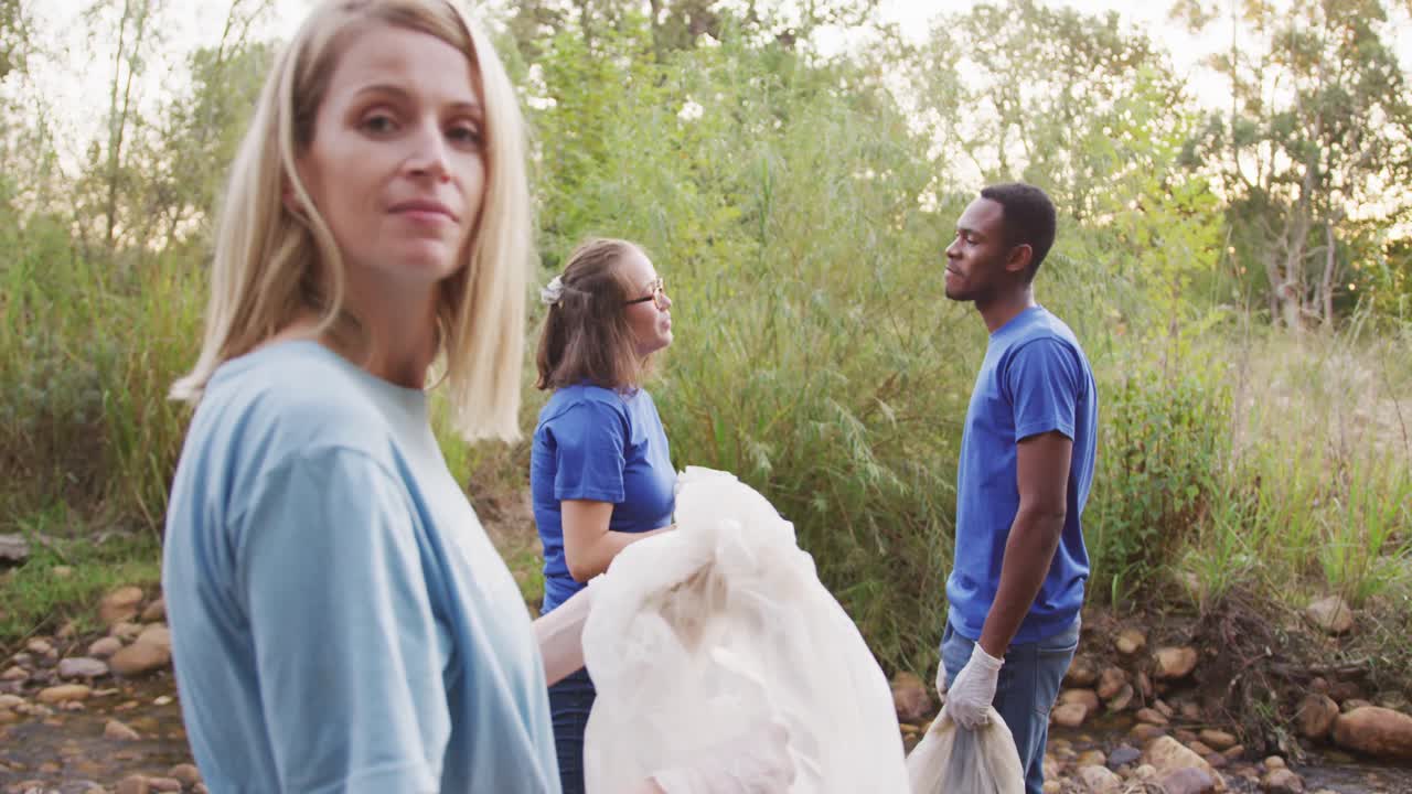 Mid adults volunteering and woman smiling at camera during river clean-up day