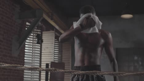 young black fighter drinking water and wiping off sweat in boxing ring