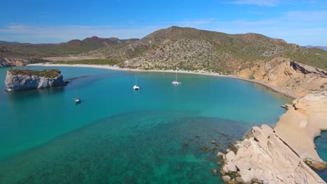 drone video flying into a beautiful protected bay of clear blue water in a tropical paradise along the coast of a rocky peninsula