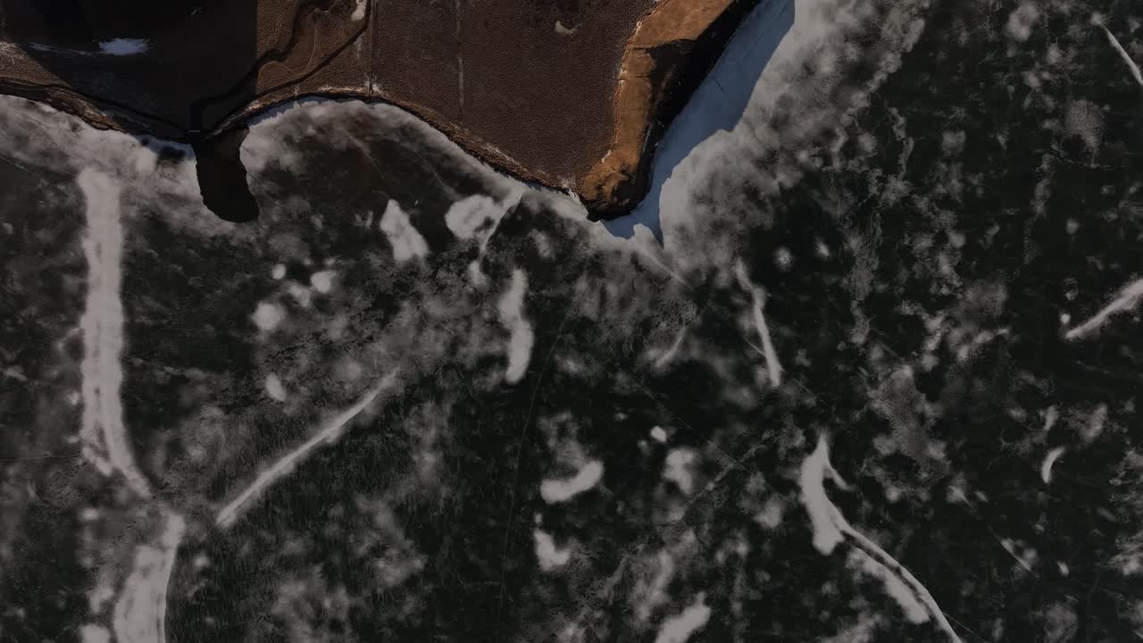 Top-down aerial of fractured lake ice and volcanic shore near Skútustaðir by Lake Mývatn. Reykjahlíð, Iceland