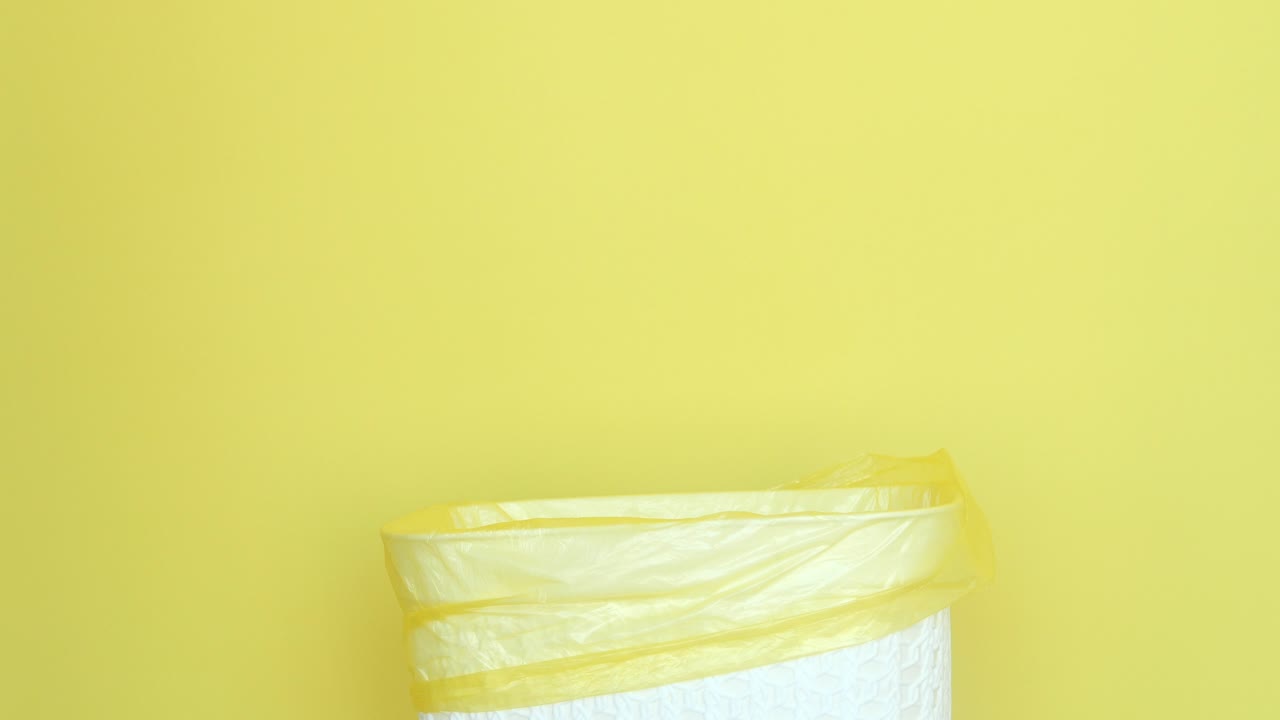 una mano lanza una manzana a un cubo de basura amarillo.