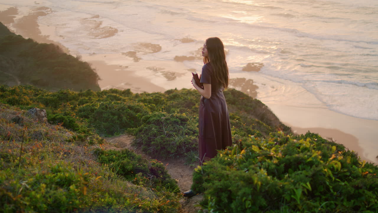 Calm brunette relaxing seashore standing hill holding book. Girl posing nature.