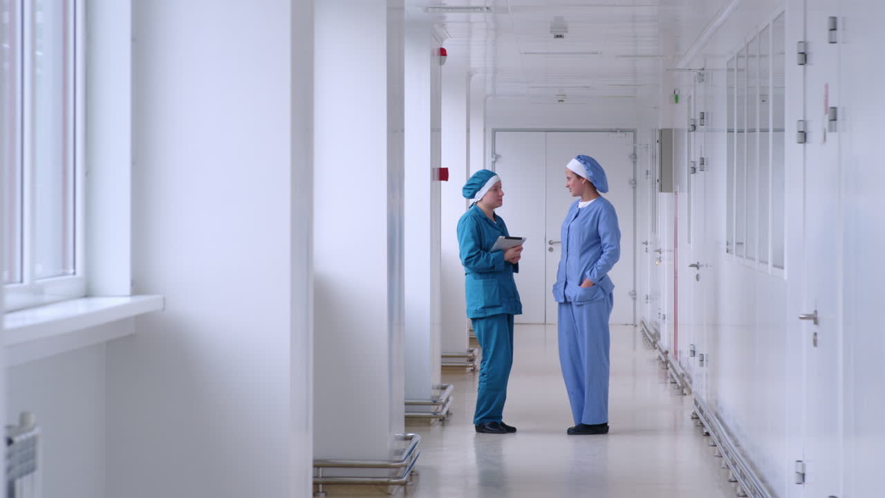 Two female workers talking in white corridor. Factory women talking