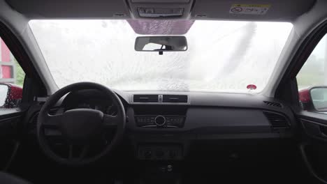 car wash interior view of man and windscreen full of white foam from high pressure cleaner