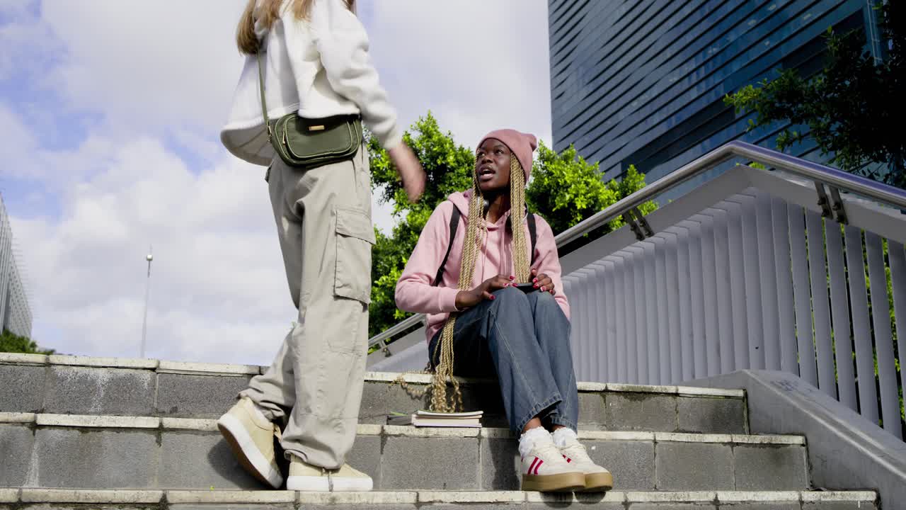 Forskellige veninder på trapper; en veninde vinker og går op, krammer og indhenter hinanden over bøger.