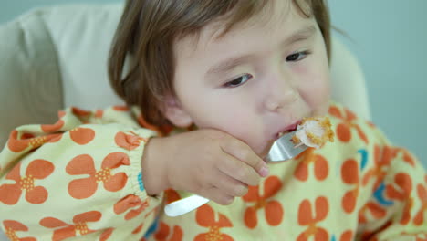 face of toddler girl eating fried chicken breast nuggets sitting in baby chair at home - close-up slow motion