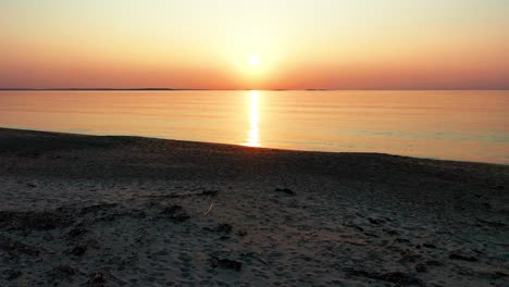 Gorgeous-Beach-Sunset-with-Bright-Glowing-Sun-Casting-Colorful-Red,-Orange,-Purple-and-Yellow-Reflections-Over-Peaceful-Rippling-Waves-of-the-Sea