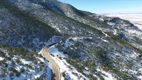 Drone-shot-following-lone-cars-on-a-snowy-desert-mountain-top-highway-during-the-daytime