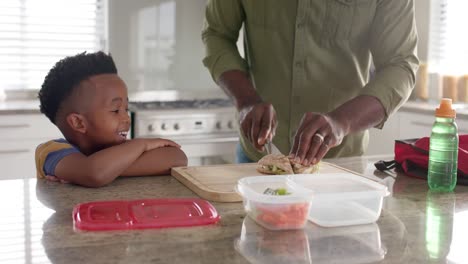 African-american-grandfather-making-packed-lunch-with-grandson-in-kitchen-for-school,-slow-motion