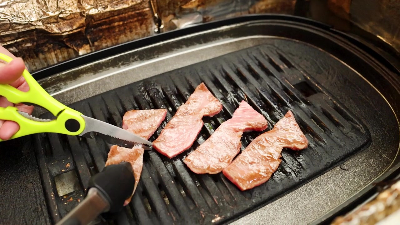 Primo piano di mani che usano forbici e pinze per tagliare la carne su una griglia a carbone