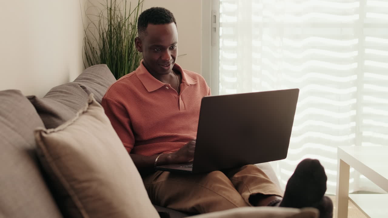 Young Black Man Smiling While Working on Laptop on Sofa