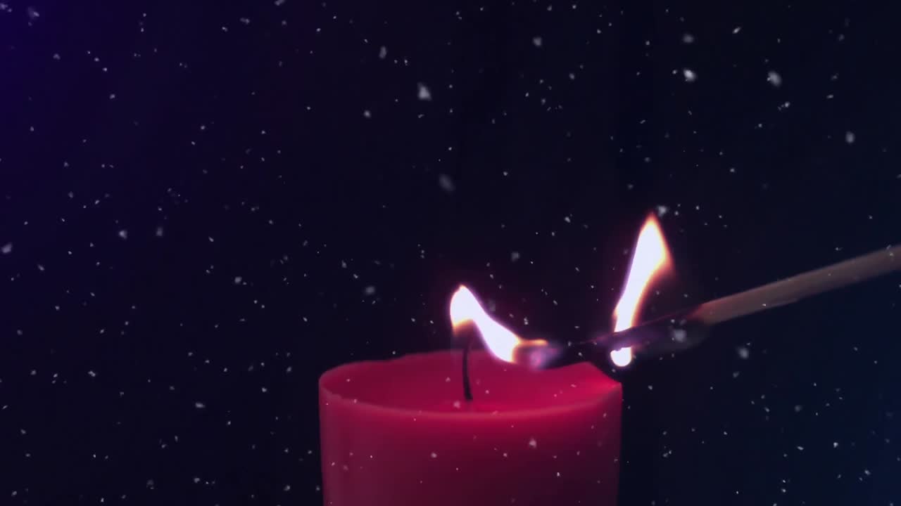 Animace padajících sněhových vloček nad sirkou zapalující červenou svíčku na černém pozadí.