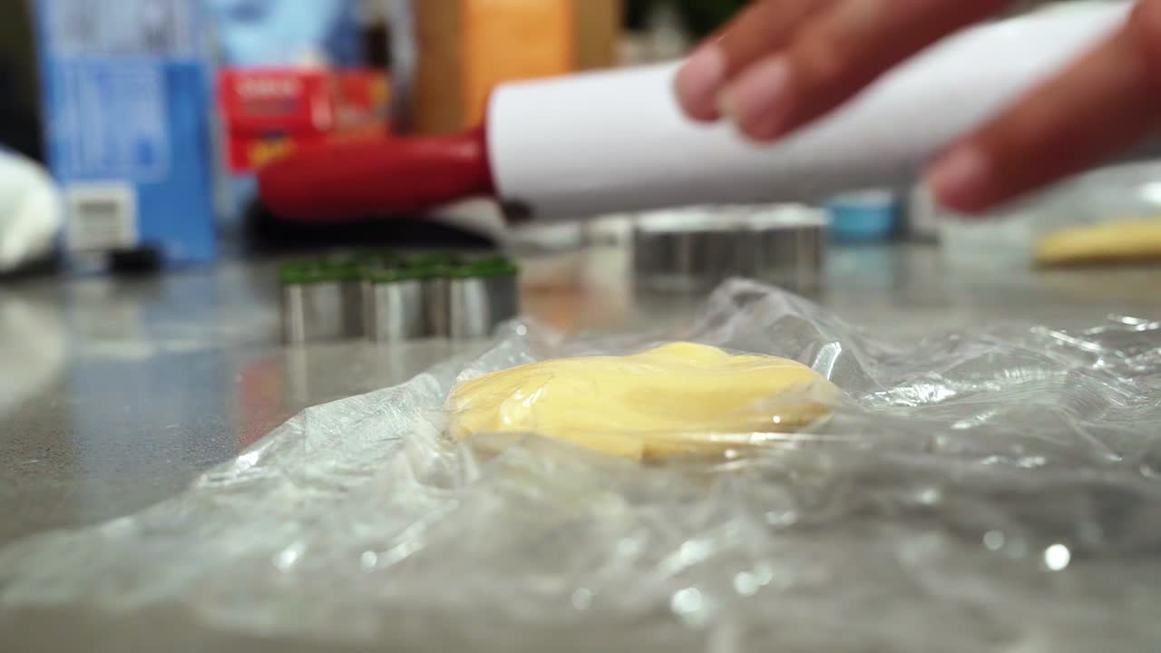 una mano triturando y aplanando una bola de masa de galleta de azúcar y luego levantando un rodillo para hacerlo más rápido para hornear galletas navideñas en una fría noche de invierno