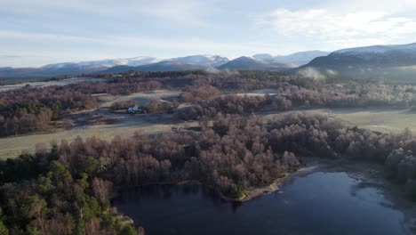 aerial drone footage of frost covered trees and forest, snow capped mountains and frozen loch in a frozen winter landscape on rothiemurchus estate in cairngorms national park, scotland