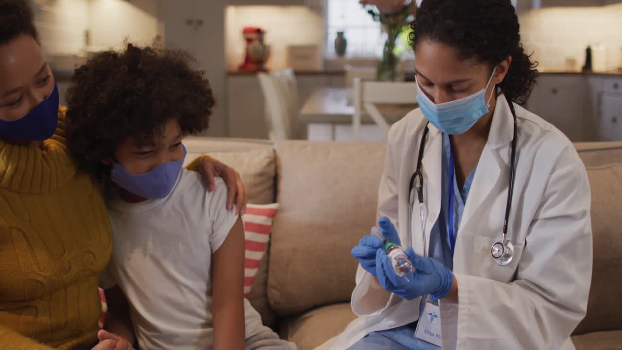Mixed race female doctor wearing face mask filling syringe at home