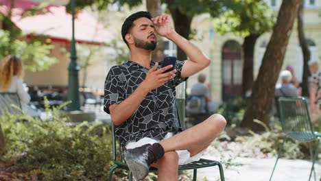 unhappy sad indian man use smartphone bad message news fortune loss game fail in city street park