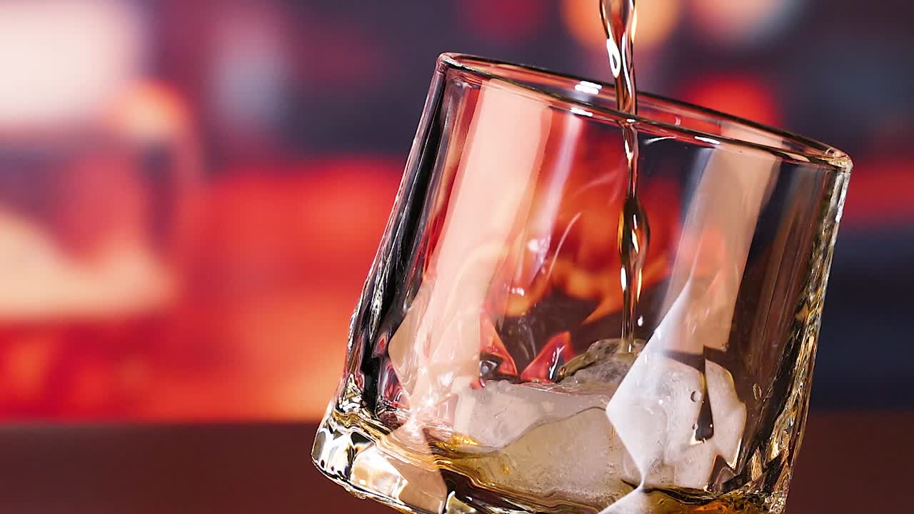 Un flusso di whiskey dorato si riversa in un bicchiere old fashioned inclinato, pieno di cubetti di ghiaccio