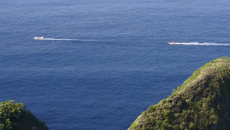 tourist boats sail on the waters around kelingking beach, nusa penida, bali, indonesia