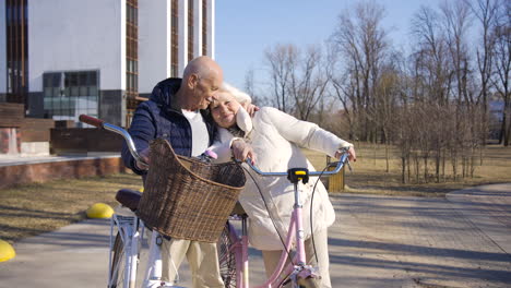 senior couple holding bikes while looking to each other, hugging and smiling in the park on a winter day