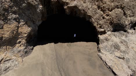 downward aerial shot of bethells beach with a man walking into the cave