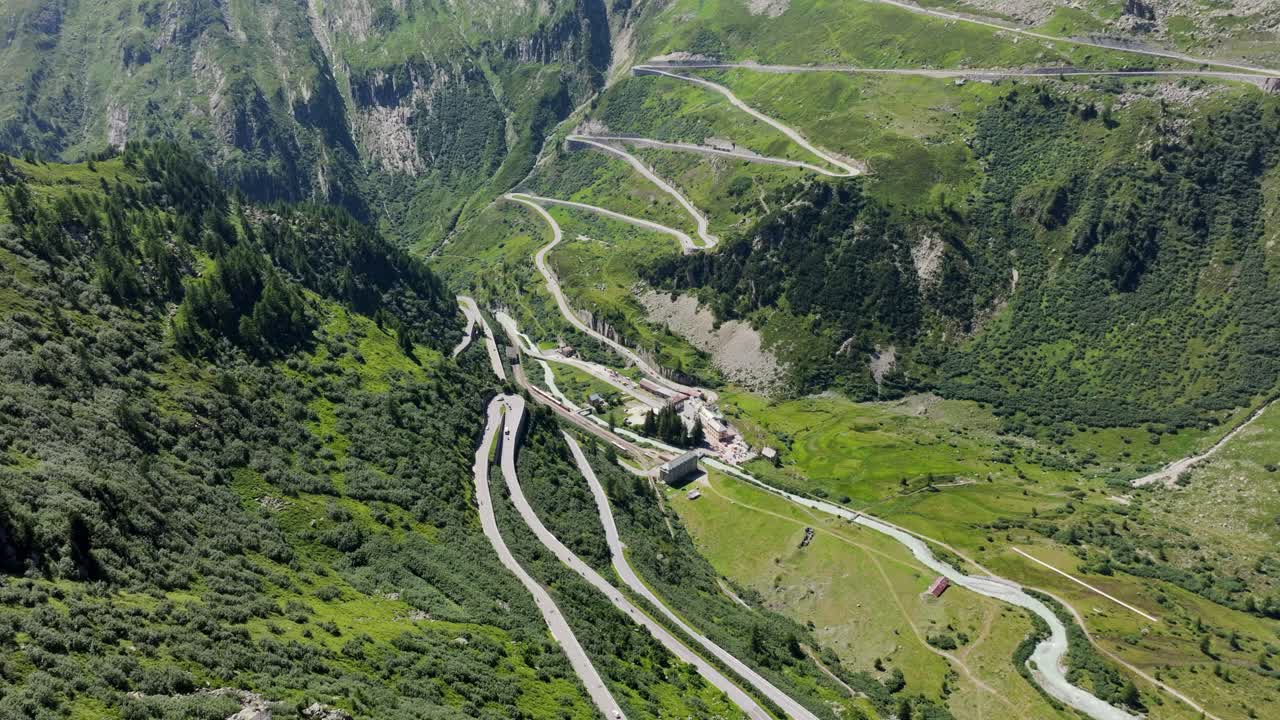 Winding mountain road cuts through lush green alpine valley warm summer daylight