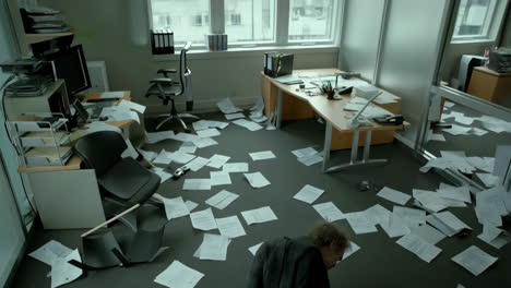 man collapsed in a chaotic office with papers scattered on the floor