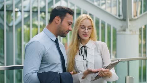 european woman with digital tablet having conversation with businessman outdoor. medium shot, slow motion