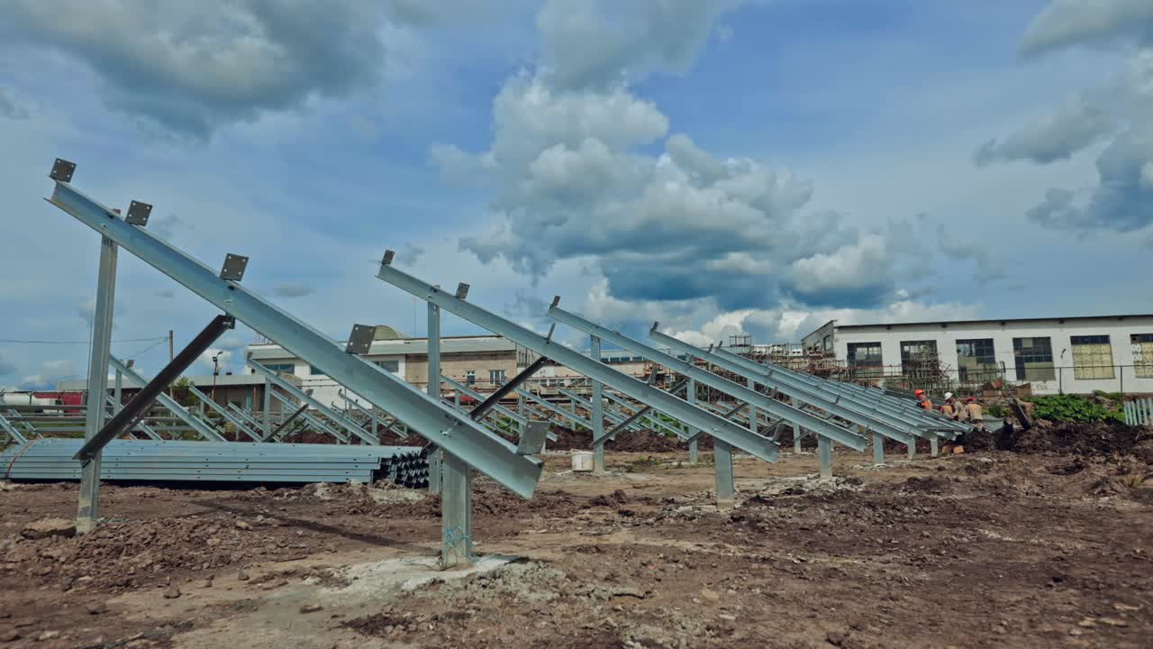 Building of a new solar farm. Teamwork of engineers constructing metal basis for solar panels under cloudy sky. Time lapse.