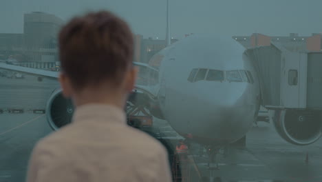 kid waiting at airport and looking at plane through the window