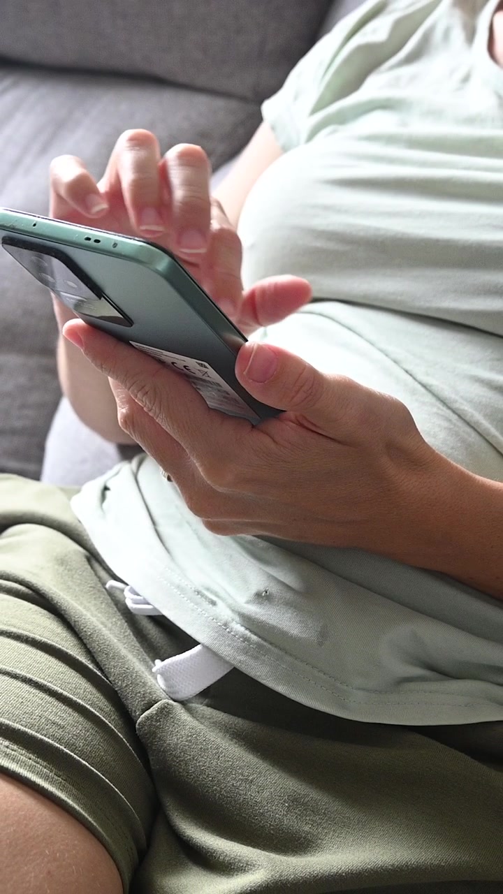 Mladá žena sedící na pohovce používá doma svůj chytrý telefon