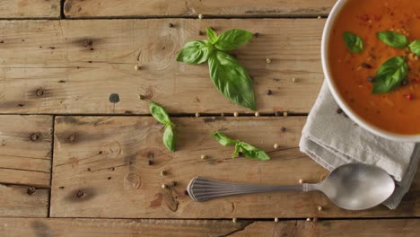 Vídeo-De-Sopa-Crema-De-Tomate-En-Un-Tazón-Sobre-Una-Mesa-De-Madera-Con-Hojas-De-Albahaca