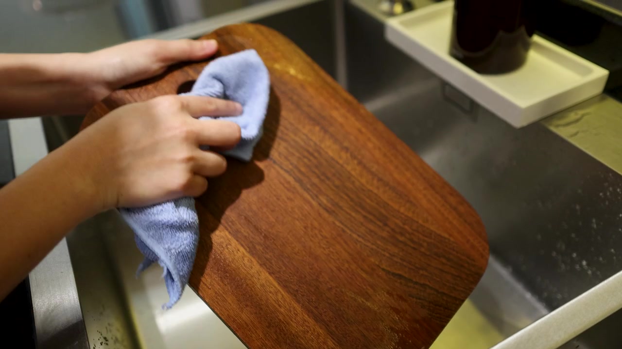 Primo piano di mani che puliscono un tagliere di legno nel lavello della cucina